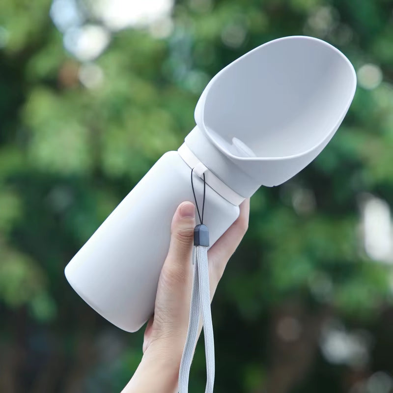 White 550 ml Sip-n-Stroll bottle held upright with wrist strap, greenery background.