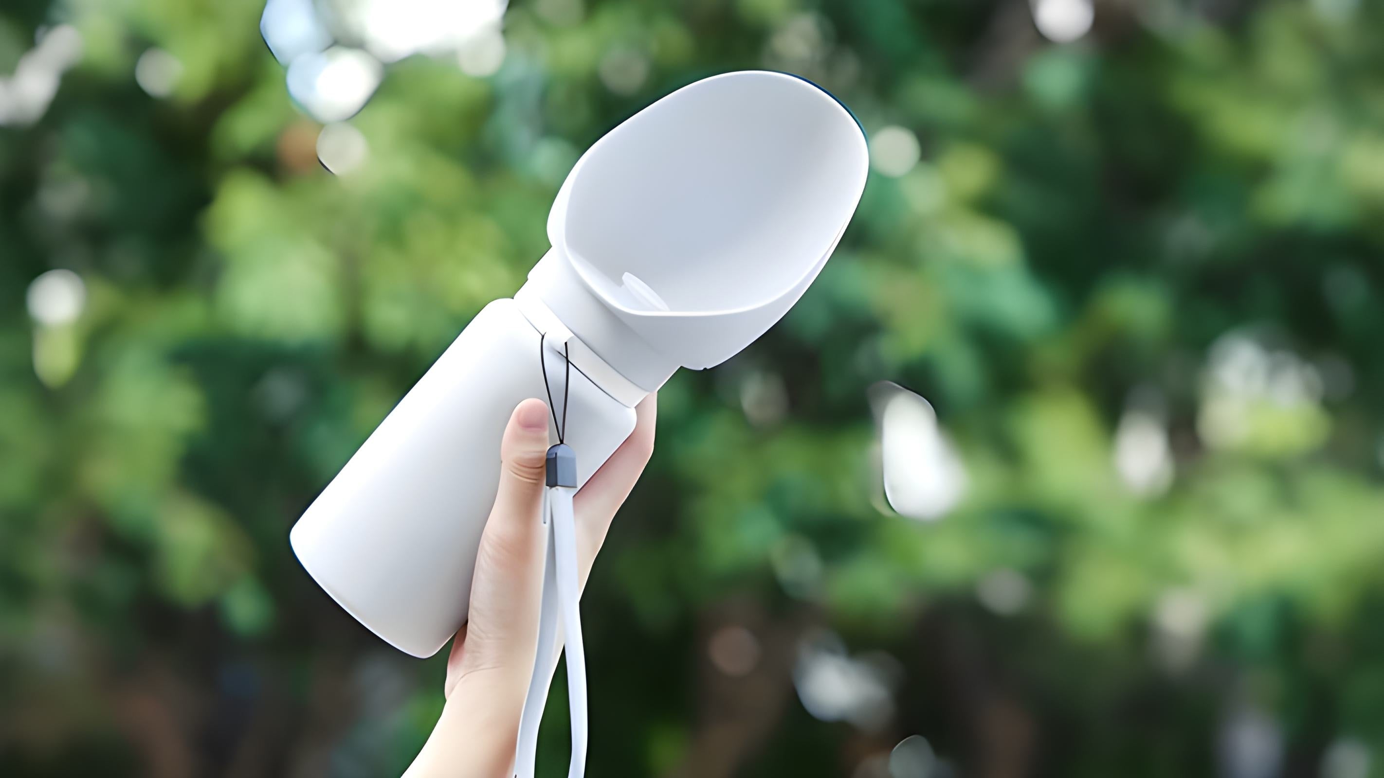 Hand holding white Sip-n-Stroll™ 550 ml portable dog water bottle outdoors — leak-proof, BPA-free travel design